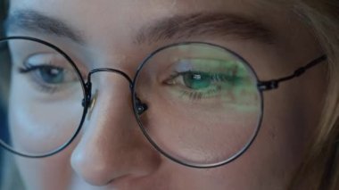 Kafkasyalı neşeli bir kadının bilgisayarın önünde oturduğu gece gözlüklü, kapalı mekanlarda yansıyan gözlüklü bir kadın.