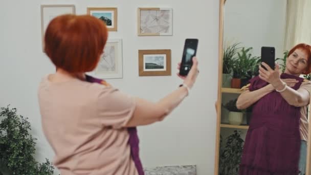 Mediana Toma Mujer Mayor Satisfecho Sosteniendo Vestido Púrpura Mirando Espejo — Vídeos de Stock