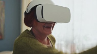 AR gözlükleri takan ve iki elinde hareket sensörleri tutan yaşlı bir kadının el sıkışması oturma odasında video oyunları oynaması.