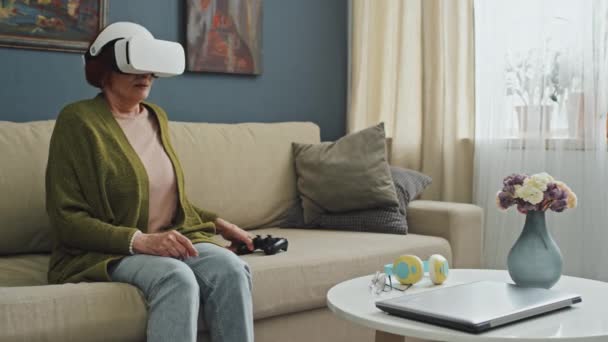 中全镜头 坐在客厅沙发上的白种人老年妇女穿着Ar护目镜玩游戏后感到疲惫 — 图库视频影像
