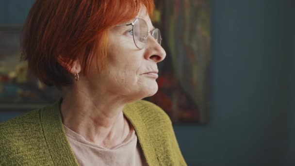 戴眼镜 头戴红头发的老年女性的中度特写镜头 在白天凄惨地回忆着过去的室内生活 — 图库视频影像