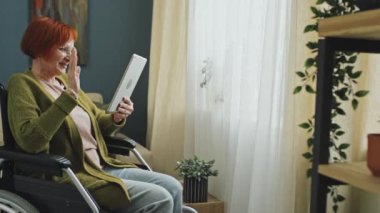 Tablet taşıyan ve video görüşmesi sırasında ailesiyle konuşan neşeli, son sınıf öğrencisi bir kadının orta solda görüntüsü.