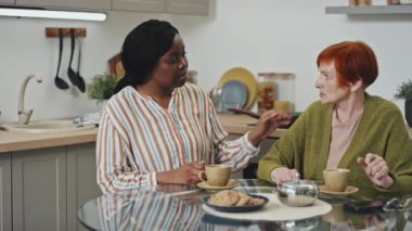 Afro-amerikalı destekçi bir kadının masada oturup, melankolik beyaz bir bayanın hislerini dinlerken orta ölçekli görüntüsü.