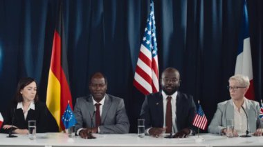 Uluslararası konferans sırasında panelde, İngiltere, ABD, AB, Almanya ve Fransa bayrakları önünde konuşan dört Afro-Amerikalı erkek ve beyaz kadın politikacının orta boy görüntüleri.
