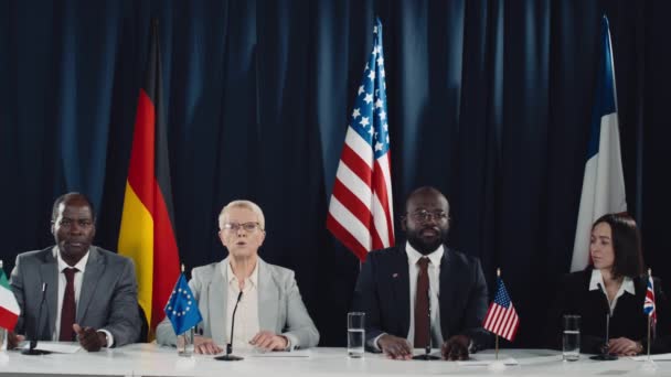 ドイツ フランス イタリア 懐中電灯の旗と 国際サミットでトリビューンに座っている4人の多様な国家指導者と 議題について話す白人女性大臣のミディアムショット — ストック動画