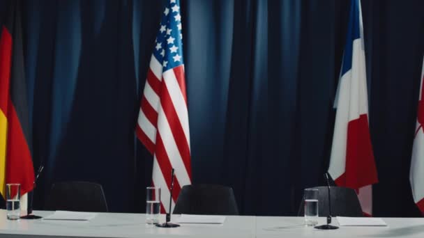 カナダ フランス ドイツ テーブル マイク 水のメガネ 背景にダークブルーのドレープの旗で国際会議のために準備された空の会議室のパンショット — ストック動画