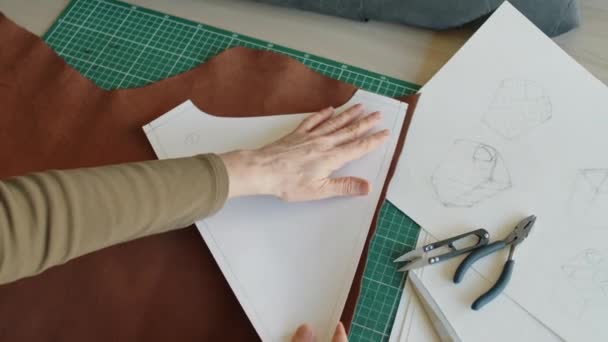 中年妇女匿名手提包设计师手的特写镜头 将剪纸贴在切碎桌上的一块棕色皮革上 将其平滑并压下去 — 图库视频影像