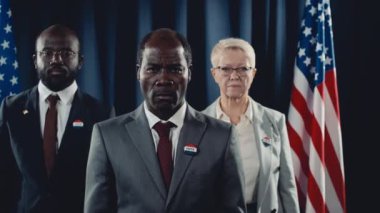 Orta yaşlı Afro-Amerikan başkan adayının orta yaşlı portresi, siyah erkek başkan yardımcısı ve Kafkas kadın basın sözcüsü, seçim kampanyası sırasında ABD bayrağı önünde poz veriyorlar.
