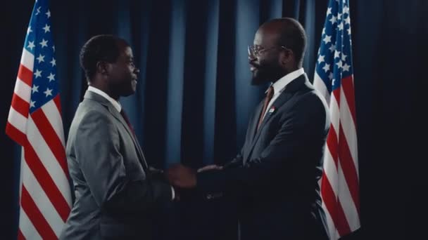陽気なアフリカ系アメリカ人政党のリーダーと黒人の男性副大統領が握手し アメリカの国旗の前に立って笑顔を浮かべ 選挙結果を祝う中 — ストック動画