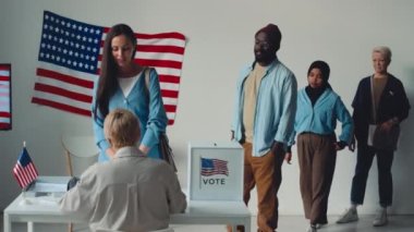 Bir grup sıradan giyinmiş Amerikalı seçim bölgesinde kuyrukta bekliyorlar. Resmi makamlara gidiyorlar, selamlıyorlar, oy veriyorlar ve kabinlere doğru yürüyorlar.