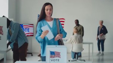 ABD eyalet seçim günü, oy sandığında, güzel beyaz kadın, Afrikalı Amerikalı erkek, tesettürlü Müslüman kadın, ABD bayrağının amblemiyle kabinde oy verdikten sonra kağıtlarını dolduruyor.