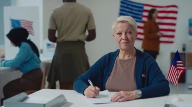 Resmi referandum sırasında seçim bölgesinde oy pusulasında çalışan gülümseyen orta yaşlı beyaz kadın belediye memurunun orta boy portresi.