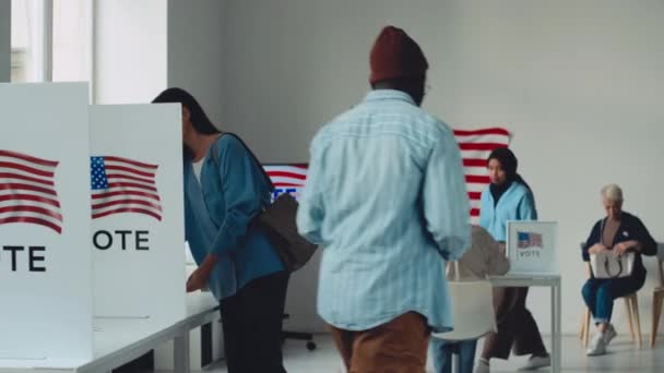多様な男性と女性のアメリカ市民のフルショットは 投票所で選挙官に歩き 投票用紙を取り 小さな立方体でそれを満たし 投票箱に詰め込んで去る — ストック動画