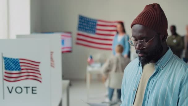 在联邦选举的投票站投票后 背景各异的人们排起了长队 身着贝尼 斜纹棉布衬衫的年轻非洲裔美国男子的中特写照片开开开心心地微笑着 — 图库视频影像