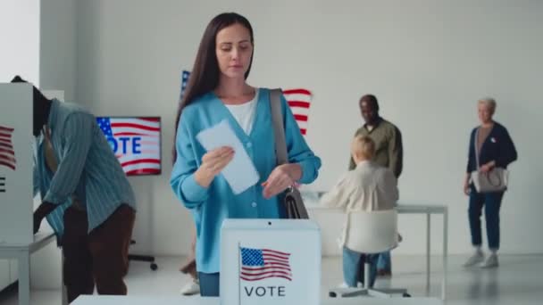 在美国州选举日的投票箱里拍到了白人美女 非裔美国男人 头戴头巾的穆斯林女士 他们拿着美国国旗在投票箱里投票后抛出了自己的选票 — 图库视频影像