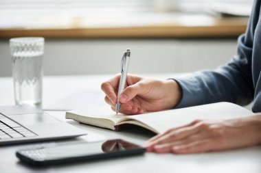 İş yerinde oturup notlar alırken elinde açık not defterinin sayfası olan genç iş kadınının eli.