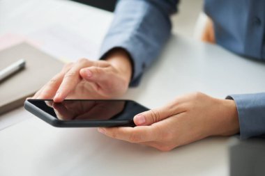 İş yerinde otururken cep telefonu ekranına işaret eden genç iş kadınının elleri ve çevrimiçi iletiler arasında kayma