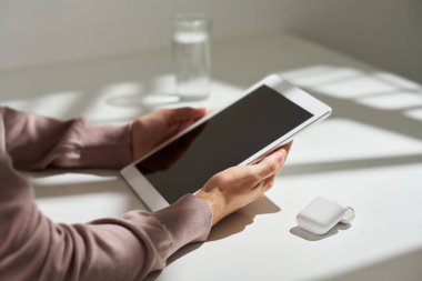 Masanın başında oturup işleri organize ederken veya internette arama yaparken bej renkli kazaklı genç bir kadının elinde boş ekranla tablet tutuşu