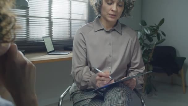 Nowoczesny Psycholog Kręconymi Siwymi Włosami Siedzący Przed Nierozpoznawalną Pacjentką Rozmawiającą — Wideo stockowe