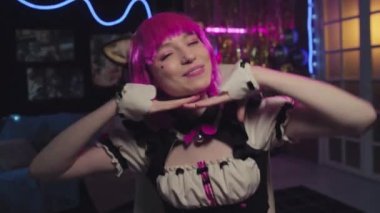 Kawaii kızının orta boy portresi. Hizmetçi elbisesi, pembe peruk ve Neko kulaklar. Kamerada poz veriyor.