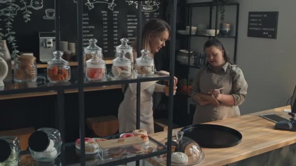 カウンターで立っている若い女性カフェ労働者は 顧客のための注文を準備しながらウェイトレスと何かを議論しながら — ストック動画