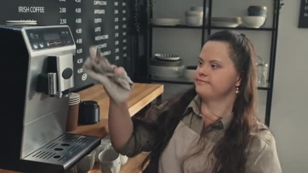 患有唐氏综合征的年轻女性咖啡师在咖啡店里工作 用干毛巾擦拭咖啡机 — 图库视频影像