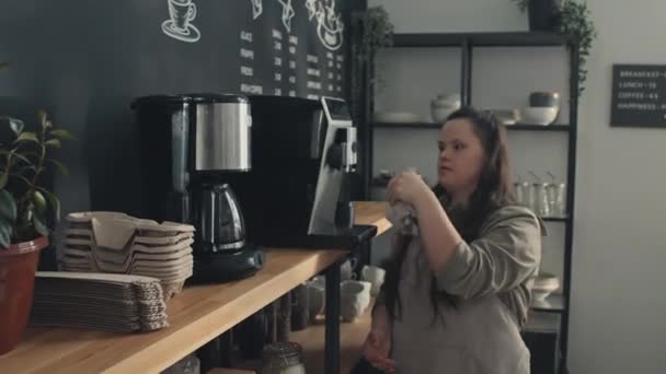 ダウン症候群クリーニングコーヒーメーカーと若い女性カフェ労働者が乾いたタオルで拭きます — ストック動画