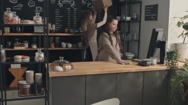 患有唐氏综合症的年轻女性和她的女同事在一家小咖啡馆里做清洁工作 — 图库视频影像