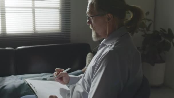 成年白种人心理治疗师在治疗期间向躺在办公室沙发上的年轻病人提问的选择性聚焦镜头 — 图库视频影像