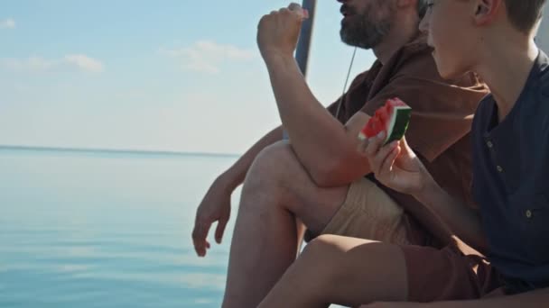 カカシア人の父親と息子は 甘いスイカを食べる帆船で晴れた夏休みの日を過ごしています — ストック動画