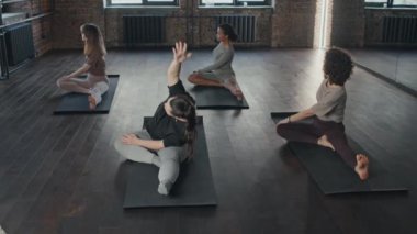 Çatı katındaki minderlerde oturan dört farklı kadının yoga egzersizi sırasında Asya esneme hareketleri.