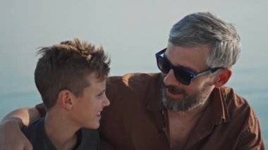 Modern beyaz adam portresi güneş gözlüğü takıyor yaz gününü dışarıda oğluyla kucaklaşıp sohbet ederek geçiriyor.