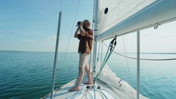 一个成熟的白人光着脚站在游艇上 用双筒望远镜遥望远方的长镜头 — 图库视频影像