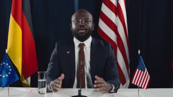 カリスマ的な中年アフリカ系アメリカ人の政治家 大統領 または政府大臣が米国旗の前にマイクでテーブルに座り 公式発表を行った — ストック動画