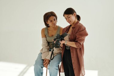 Kültürler arası şık giyinmiş iki genç kadın fotoğraf çekimi sırasında birinin fotoğraf makinesinde çektiği yeni fotoğrafları tartışıyor.