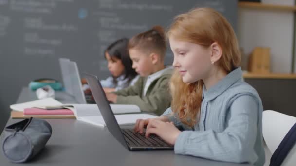 学校の教室で机に座って 昼間にラップトップのキーボードに何かを入力する小学生のミディアムショット — ストック動画