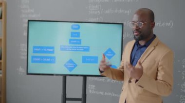 Afrika kökenli Amerikalı bir erkek öğretmenin elinde tablet tutarken ve gündüz okuldaki konferans sırasında ekranda diyagramı açıklarken orta boy görüntüsü.