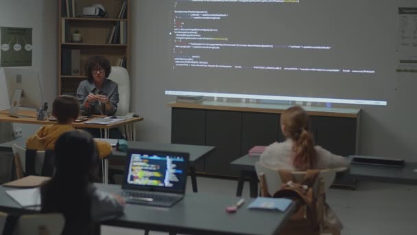 プログラミングレッスン中に小学生と議論しながら教室で机に座っている白人女性教師のフルショット — ストック動画