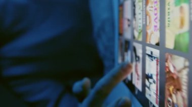 Tabletle masada oturan ve gece vakti içeriden izlemek için film seçen tanınmamış bir kadının yakınına.