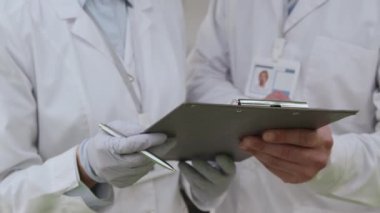 Beyaz erkek ve Asyalı kadın laboratuvar çalışanlarını yakın çekimde belge okuyup tartışıyorlar.