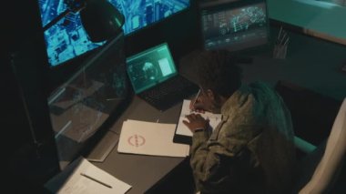 Yüksek açılı, odaklanmış Afrika kökenli Amerikan askeri gözetim memurunun izleme programıyla ekranlara bakarken görüntüsü.