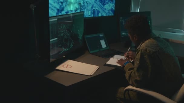 監視プログラムを見て メモを作るコンピュータ画面の前に座っている男性のアフリカ系アメリカ人軍人労働者のフルショット — ストック動画