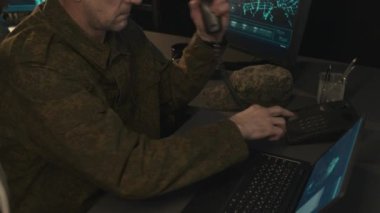 Beyaz erkek askeri gözetim memurunun dizüstü bilgisayarda oturup klavyeye yazı yazarken ve gece acil bir telefon görüşmesi yaparken çekilmiş.