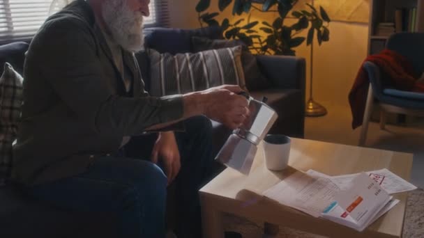 清晨时分 一位白发苍苍 留着白胡子的中杯白人老人坐在昏暗的沙发上 把新咖啡从莫卡壶倒进杯子里 然后喝了下去 — 图库视频影像