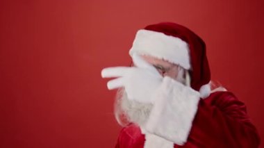 Noel Baba 'nın kırmızı takım elbiseli, sivri şapkalı ve gözlüklü gri saçlı, sakallı ve bıyıklı Batman hareketleriyle kırmızı arka planda enerjik bir şekilde dans ederken orta boy yakın çekimi. Şablon, boşluğu kopyala
