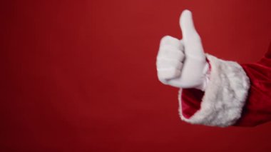 Beyaz eldivenli isimsiz Noel Baba 'nın kırmızı arka planda elini uzatıp başparmağını kaldırdığı yakın plan fotoğrafı. Kopyalama alanı, şablon kadar uygun