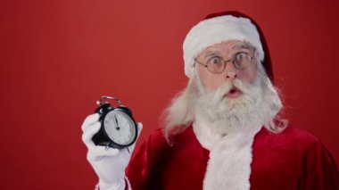 Noel Baba 'nın gece yarısı alarmlı saati işaret ettiği orta ölçekli kapalı çekim. Omzunun üzerinden hediyeler atan ve kırmızı arka planda ayrılan çanta. Şablon, boşluğu kopyala