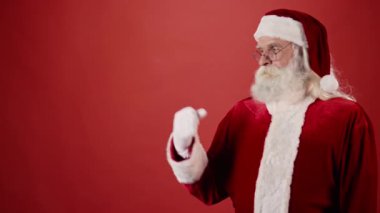 Geleneksel ceketli yaşlı Noel Baba 'nın bir şeyi tutmak için elini uzattığı, kameraya bakıp kırmızı arka planda gülümsediği orta boy bir fotoğraf. Uzayı kopyala, şablon