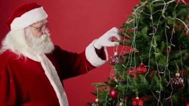 Noel Baba kıyafetli, gözlüklü, gri sakallı ve bıyıklı orta yaşlı adamın Noel süslerini dikerken orta boy fotoğrafı. Şablon, boşluğu kopyala