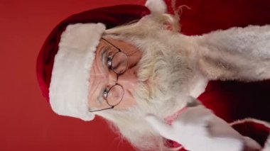 Noel Baba 'nın kırmızı ceketli, şapkalı ve gözlüklü gri sakallı ve bıyıklı, kameraya bakan, kaşlarını çatan ve parmağını sallayan orta boy dikey görüntüsü. Şablon kadar uygun, alanı kopyala